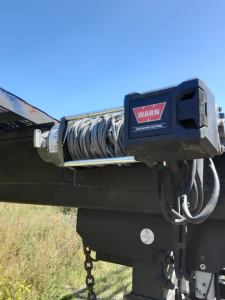 Winch mechanism on a car carrier trailer with coil cable and a WARN winch label visible.