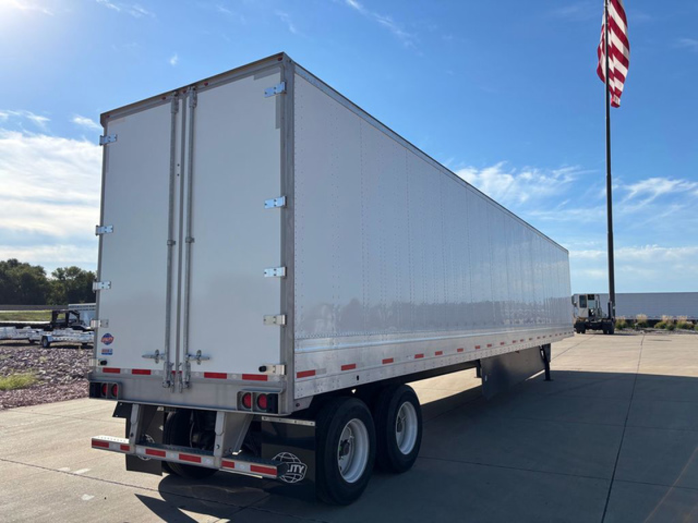 Trailer side and rear view showing a long aluminum utility trailer with dual rear doors and tandem axles.