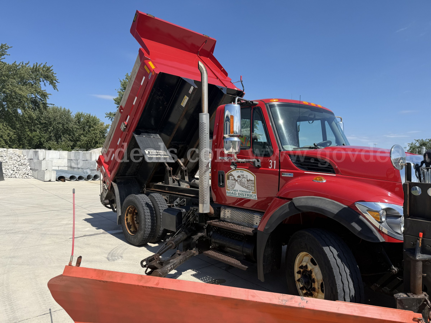 International dump truck with red cab and raised red dump body, side view showing crane/arm and wheel areas; no legible text clearly visible on truck body in this image.