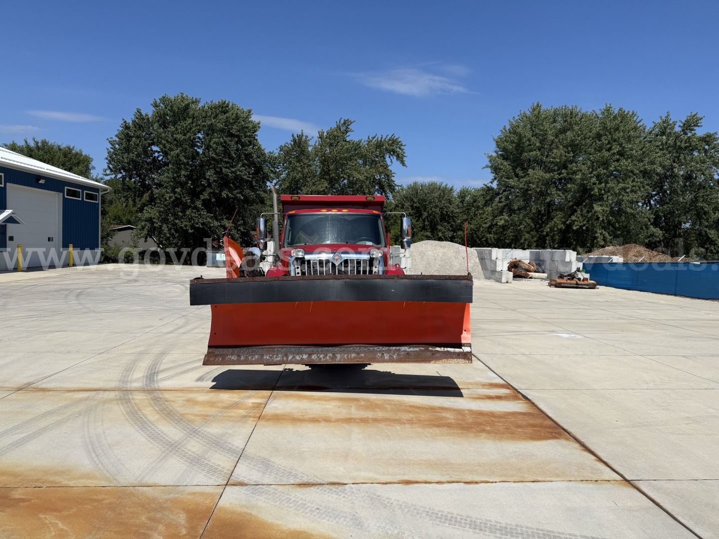 Truck in a lot with a front-mounted snowplow blade attached, International 7400 dump truck seen from front, clear sky