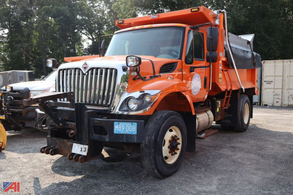 Dump truck in orange showing front grille and cargo bed with headlights; International WorkStar badge and blue license plate visible.