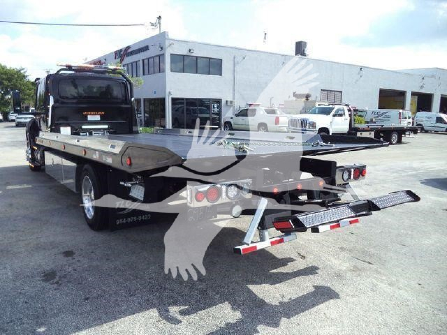 2027 International MV rollback truck on trailer with rear loading ramps and flatbed; dealership lot in background with other trucks and a white building.