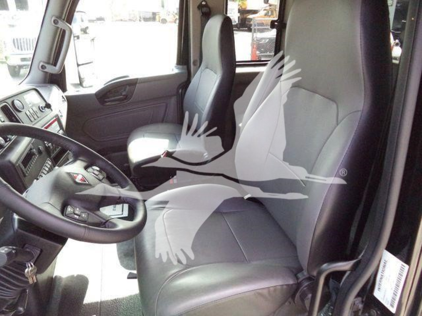 Cab interior of a 2027 International MV truck showing driver seat, steering wheel, and passenger seat in view with light gray upholstery.