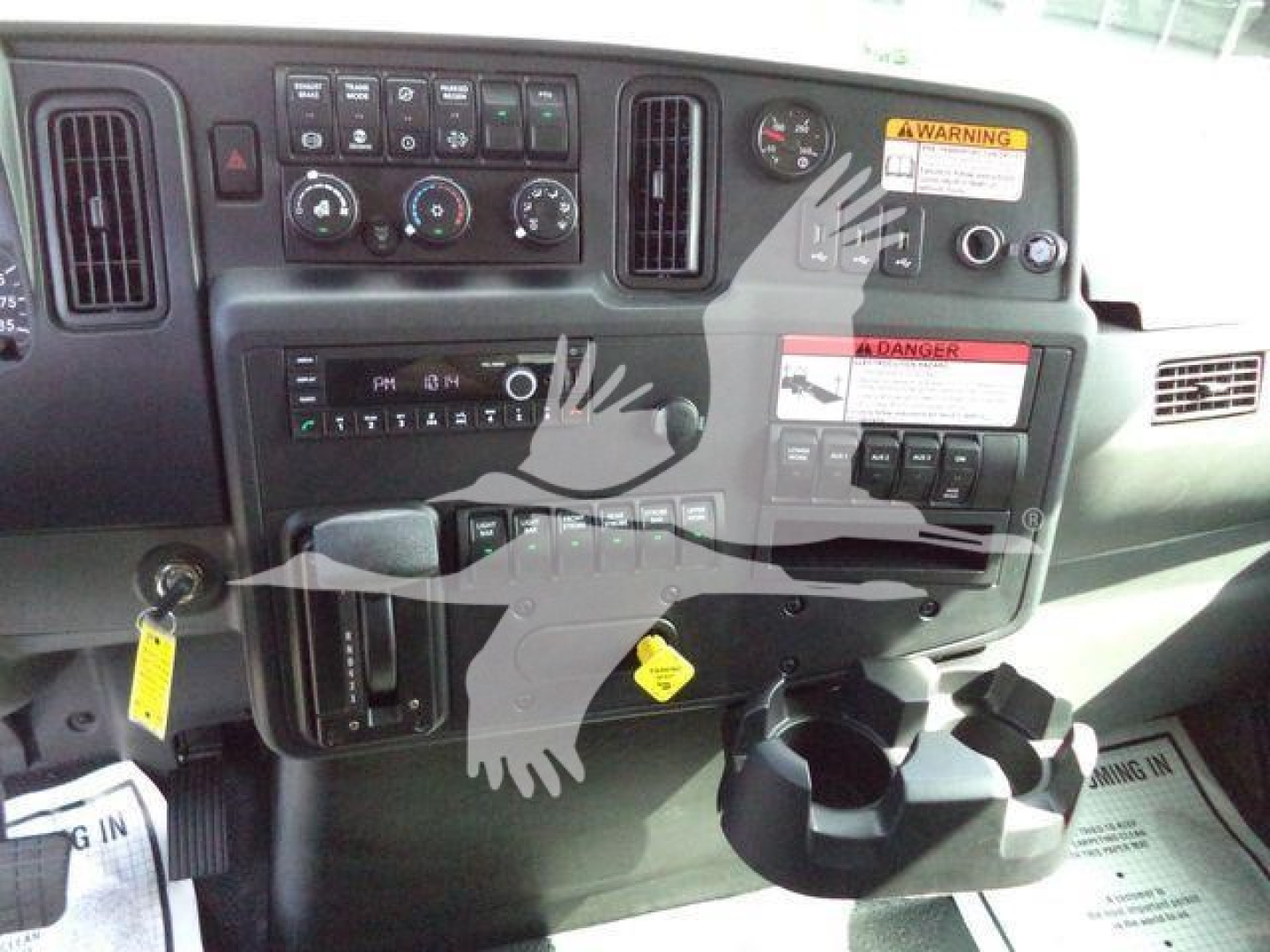Dashboard and control panel of a 2027 International MV truck showing gauges, switches, cup holder area and warning labels.