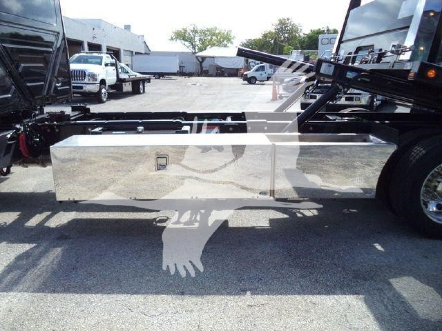 Flatbed truck chassis side view with polished aluminum toolbox mounted beneath the cab, International MV truck frame in yard.