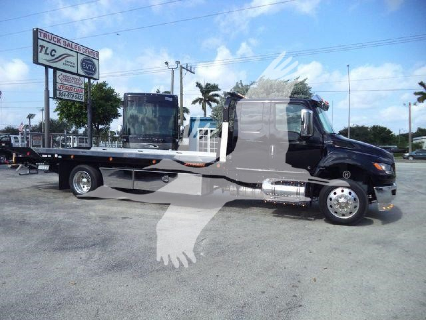 Flatbed tow truck in a dealership lot, black cab with chrome accents, MV607EXCAB22ITD stock number visible, rollback category, International MV model.