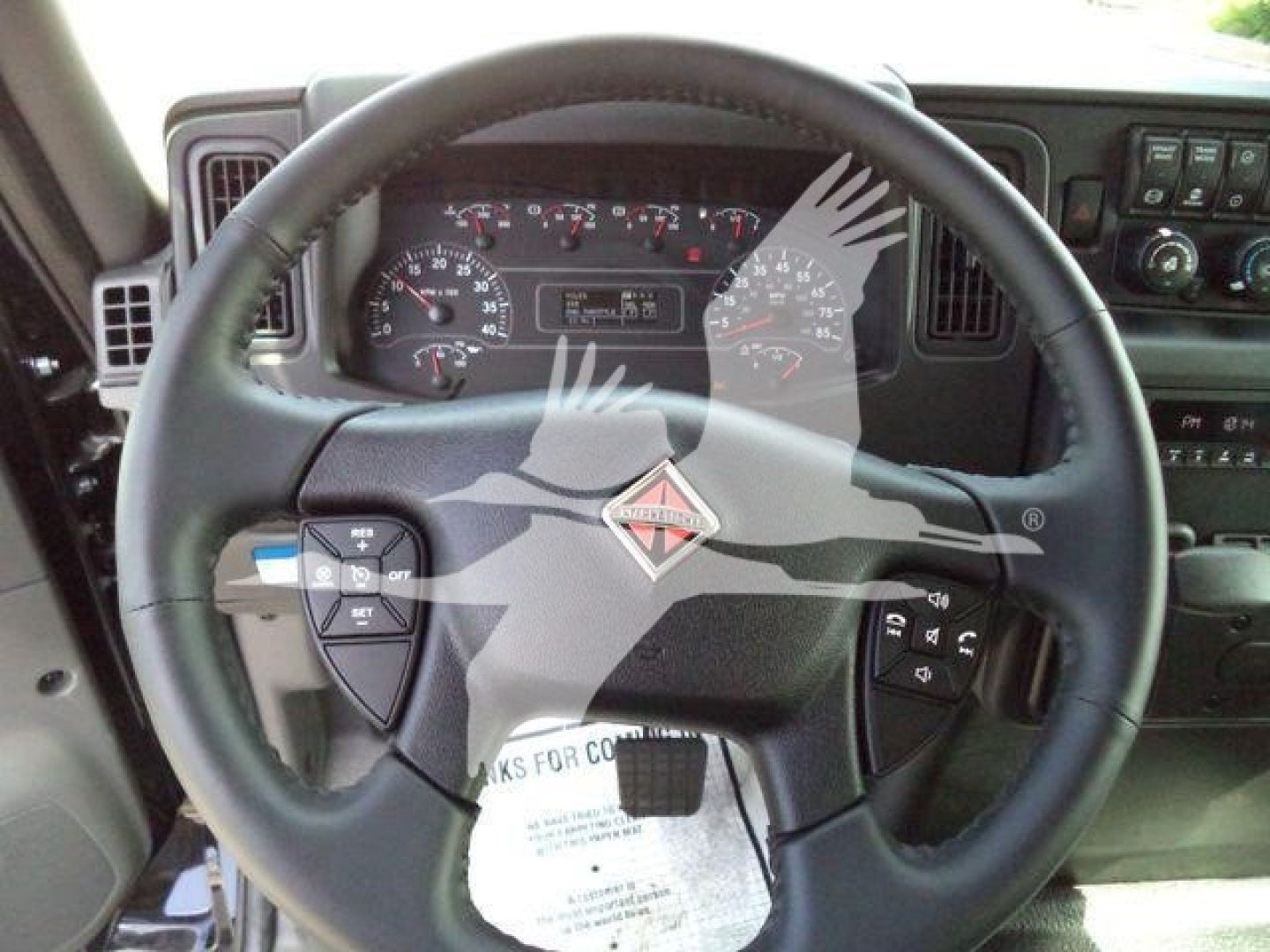 Interior of a 2027 International MV truck cab focusing on the steering wheel with dashboard gauges and control stalks visible.