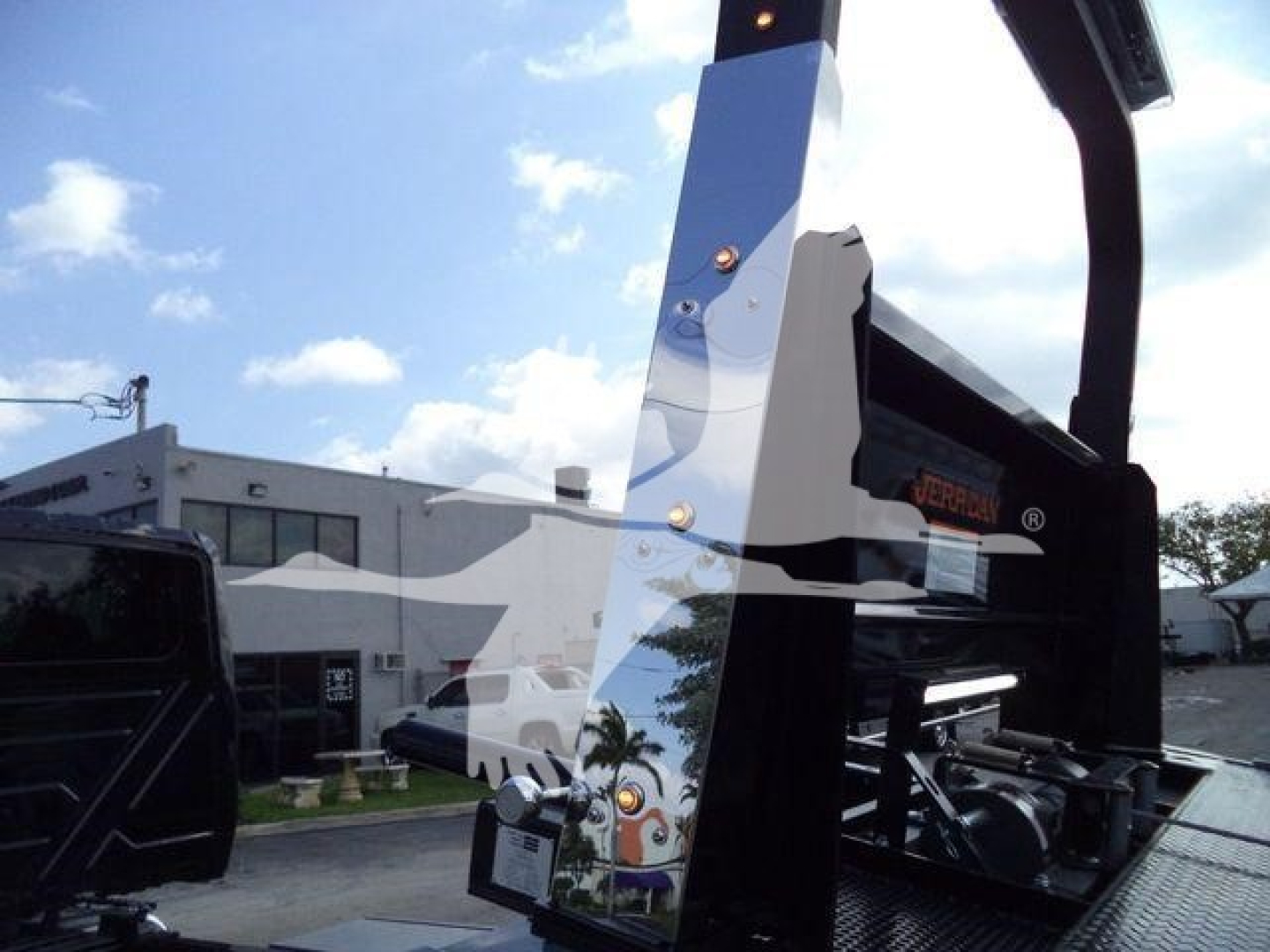 Rollback truck equipment showing vertical steel frame with hydraulic components and a reflection of a warehouse in the chrome surface; part of a 2027 International MV listing.