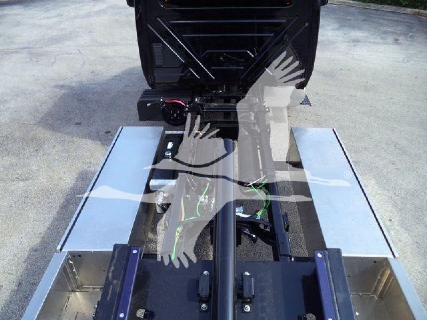 Truck chassis and hydraulic rollback setup with metal side rails and exposed wiring harness seen from rear perspective.