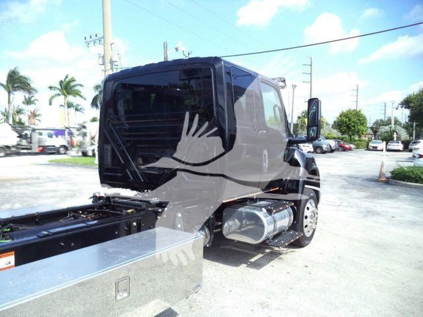 Side view of a black International MV truck in a dealership lot, showing the cab and fuel tank with reflection of palm trees in a sunny sky.
