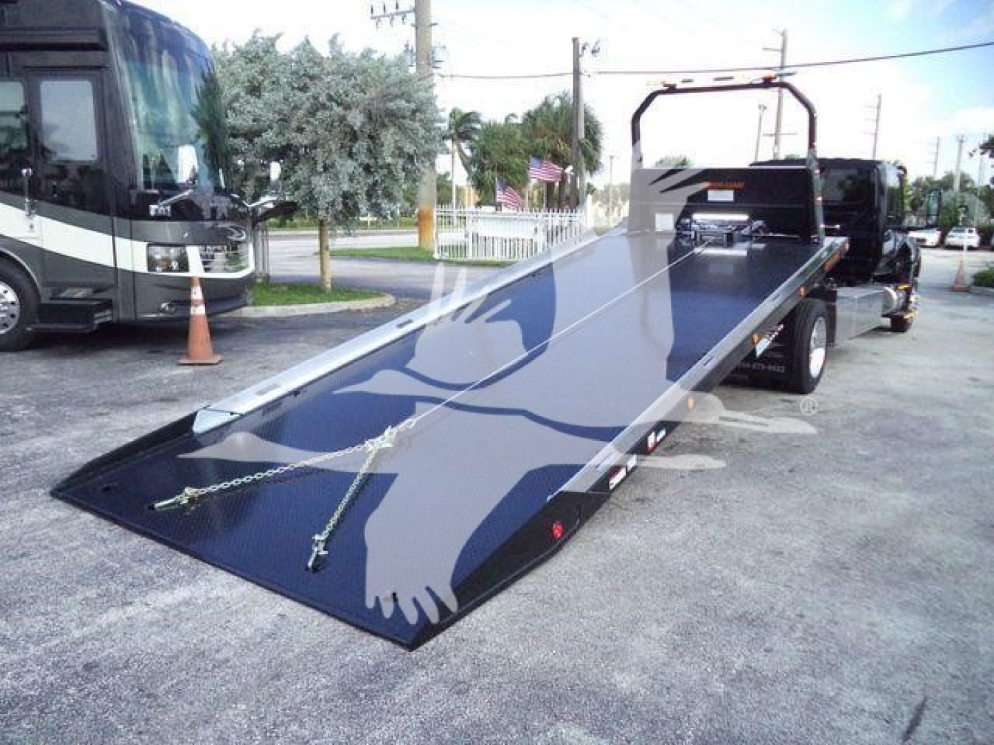 Tractor trailer tow truck with a long black fold-down ramp in a dealership lot. MV607EXCAB22ITD stock number visible in listing; rollback truck category.