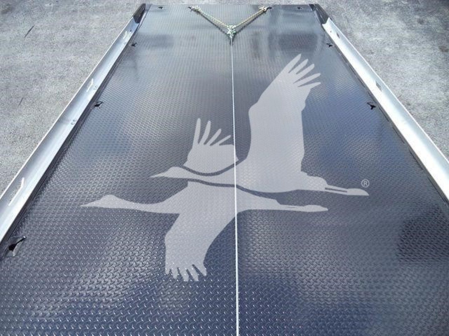 Platform deck with textured black diamond plate showing a large white graphic of two flying birds in formation, with a seam in the middle and a chain secured at the top.