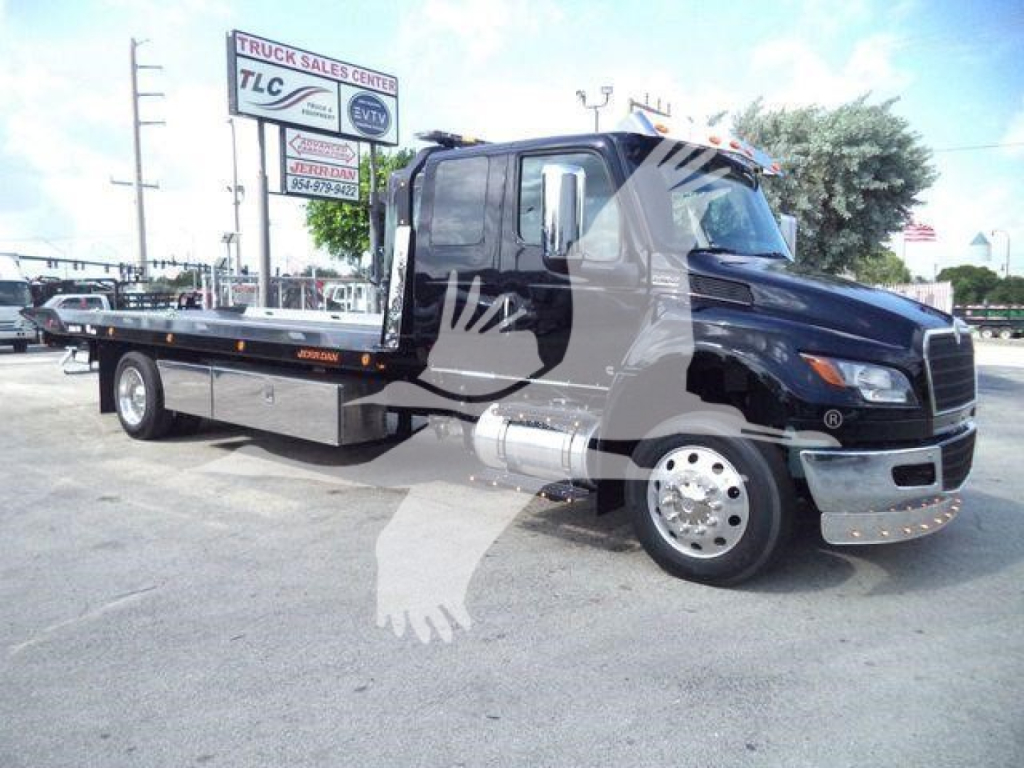 Tow truck with flatbed on a black cab, side view showing chrome bumper and dual rear wheels, dealership lot in background.