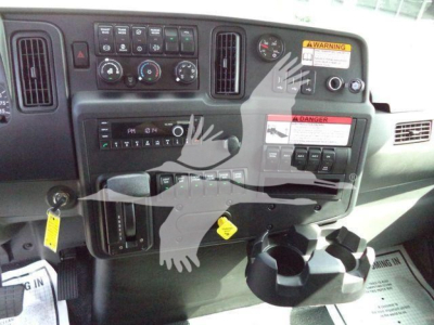 Dashboard and control panel of a 2027 International MV truck showing gauges, switches, cup holder area and warning labels.