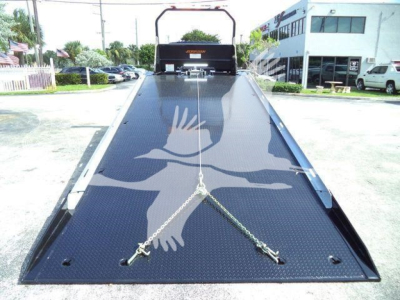Flatbed truck loading ramp with chains and steel diamond plate, International MV series in background.