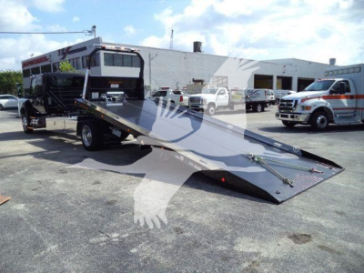 Tow truck rollback bed extended with International MV cab and flatbed ramp visible in front, service yard in background.
