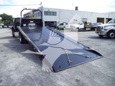 Tow truck rollback bed from side angle showing ramp with chains and black textured surface.