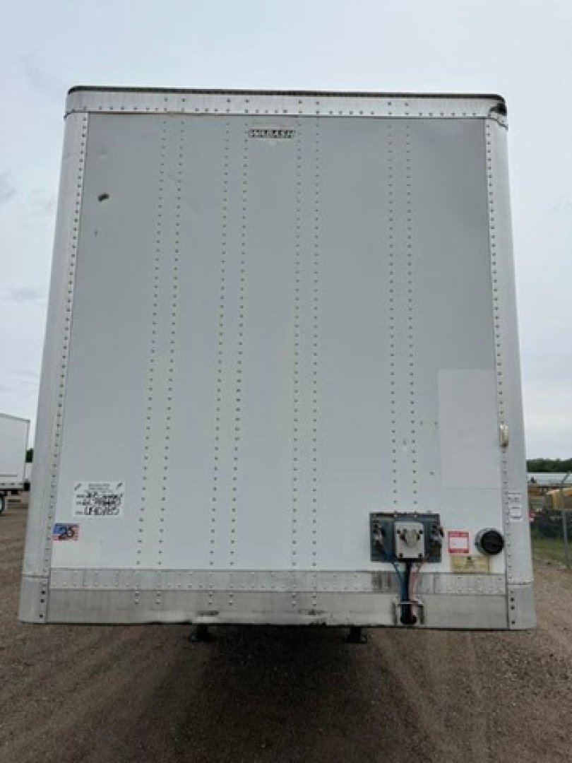 Rear view of a white 2013 Wabash van trailer showing riveted metal panels and rear doors with a blue electrical connector and warning stickers.