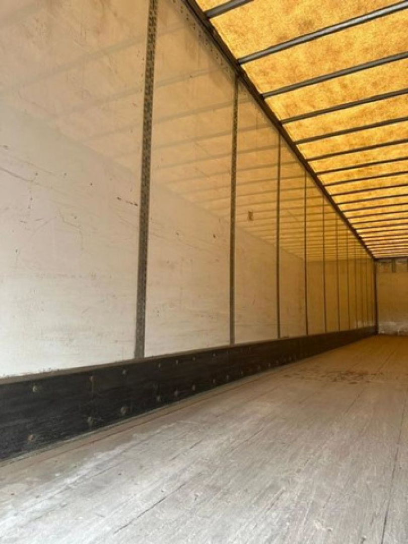 Trailer interior showing long cargo area with white walls, ribbed steel framing, and wooden floor planks.