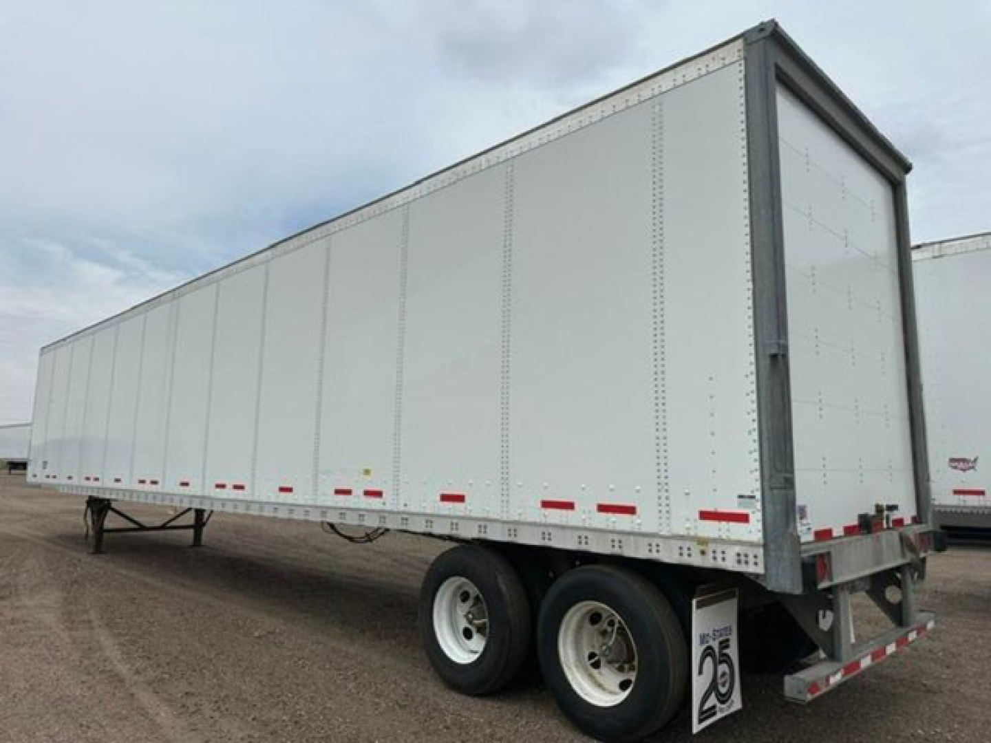 Trailer side view showing a white Wabash van trailer with dual rear wheels and reflective tape along the lower edge.