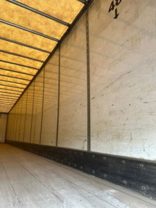 Truck trailer interior with white side panels and ribbed ceiling; faint black marks along the base; numbered markings near top right reading '40' and a vertical line.