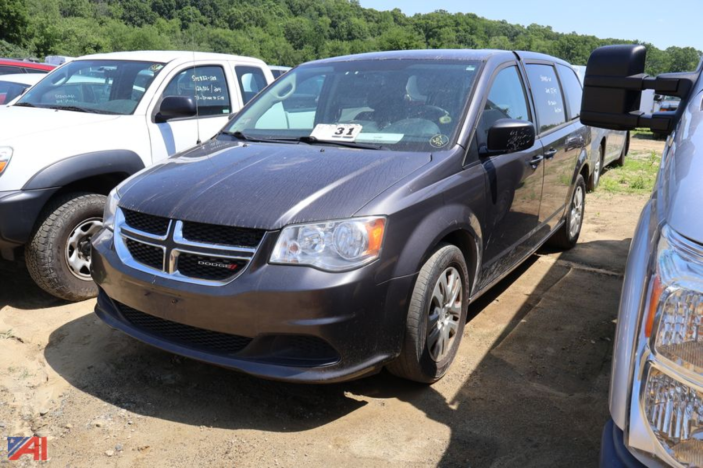 Dodge Grand Caravan minivan in a used vehicle lot, front-left view with other vans nearby and a dirt lot.