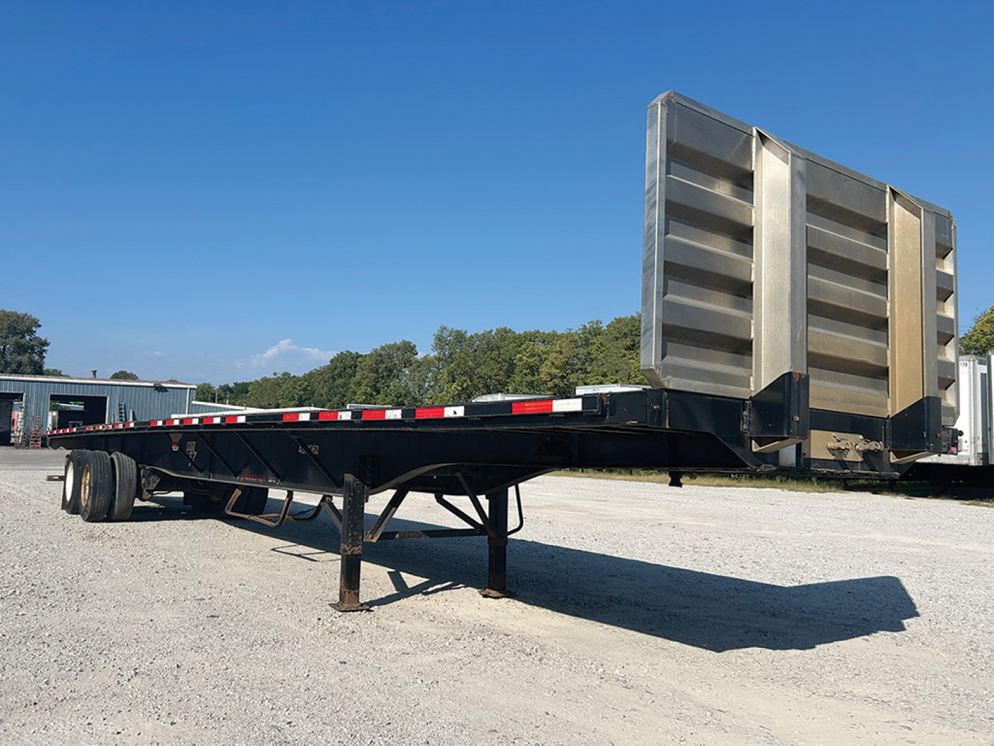 Trailer frame and raised dump box of a 2017 Transcraft 554 S flatbed trailer with metal stake sides in a gravel lot.