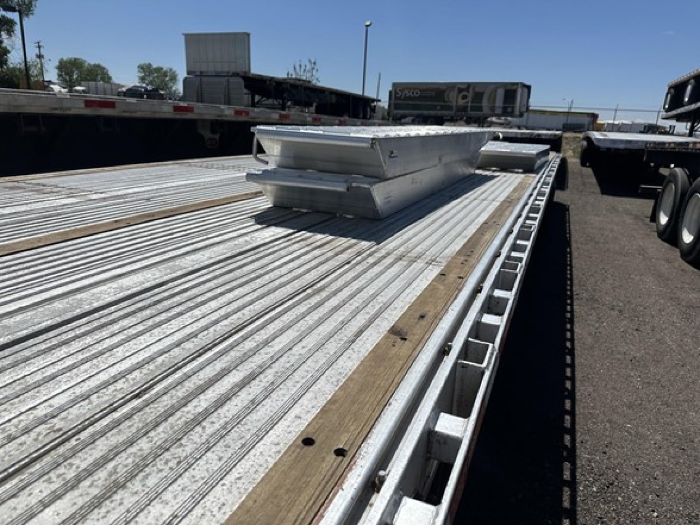 Aluminum drop deck trailer showing ribbed deck with two tool boxes and a raised maintenance step in view
