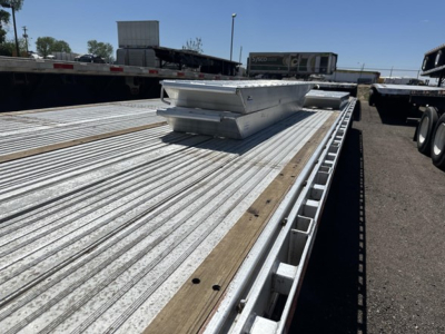 Aluminum drop deck trailer showing ribbed deck with two tool boxes and a raised maintenance step in view