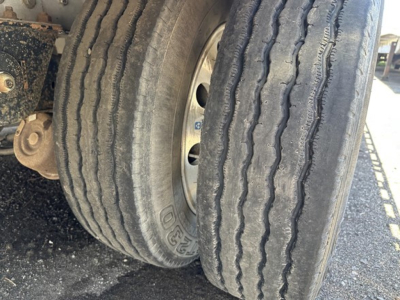 Trailer wheel and tire close-up showing dual tires and part of aluminum drop deck trailer.