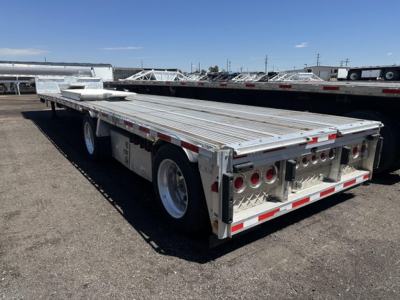 All-aluminum drop deck trailer showing two side-by-side ramps and tool boxes, with rear dual axles and multiple round tail lights.