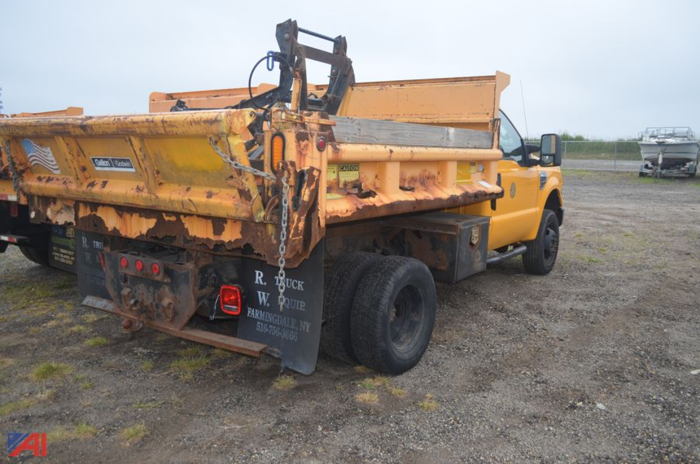 Ford F-350 Super Duty dump truck with plow rear view showing yellow dump bed and hydraulic mechanism, DOT trailer hitch, and worn black mud flaps with white text.
