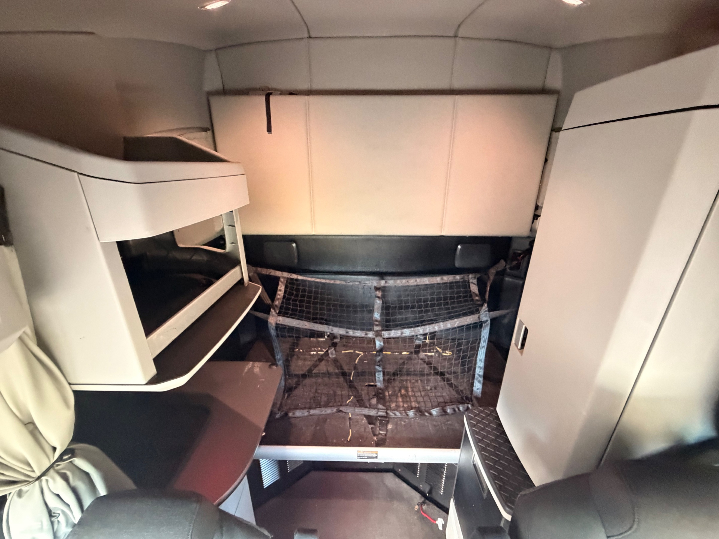 Kenworth T680 sleeper cab interior showing upper bunk, storage cabinets, and a doghouse area with metal grate floor.