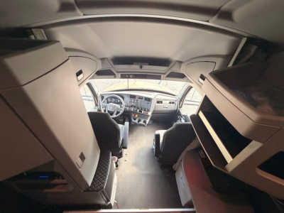 Interior of a Kenworth T680 cab, front dashboard and seating visible from rear; overhead storage compartments on both sides.
