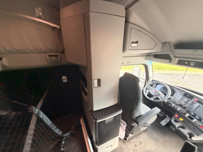 Kenworth T680 cab interior showing driver seat and dashboard with sleeper storage cabinet and overhead compartments.