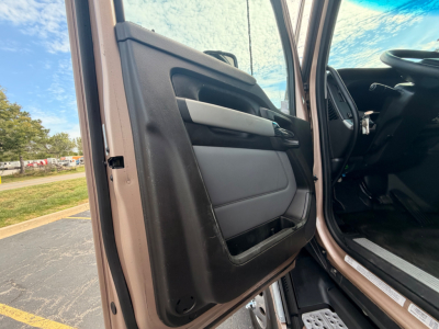 Truck cab interior door panel view with beige and black materials; steering wheel visible in distance; open door.