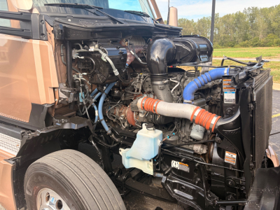 Kenworth T680 engine bay showing turbo intake, blue coolant reservoir, orange and white silicone hoses, and various engine components.