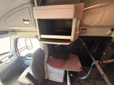 Cab interior showing a flip-out tray and a mounted tablet/computer screen with space behind, passenger seat visible, hanging cords, and a partition grid to the right.