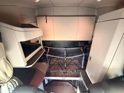 Kenworth T680 sleeper cab interior showing upper bunk, storage cabinets, and a doghouse area with metal grate floor.