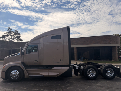 Kenworth T680 conventional sleeper truck side view showing dual rear axles and cab high-roof with beige color and chrome wheels.