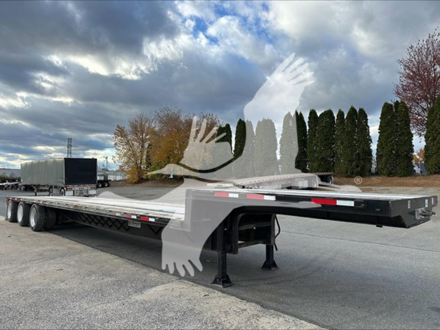 Low-angle view of a 2016 Transcraft DTL-2000 drop deck trailer showing long flatbed with multiple axles and a lowered neck area.