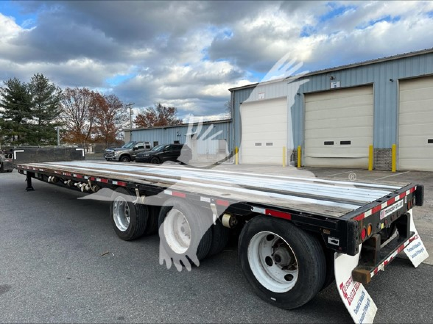 Transcraft DTL-2000 drop deck trailer in serviceable condition, dual rear axles, long flatbed with reflective tape and wheel chocks, rear lights and mudflaps visible.