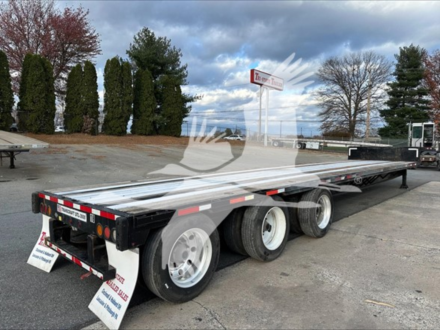 Tri-axle low-profile drop deck trailer showing DT L-2000 style with tandem axles and aluminum deck. Side rails. Reflective tape and rear lights visible.