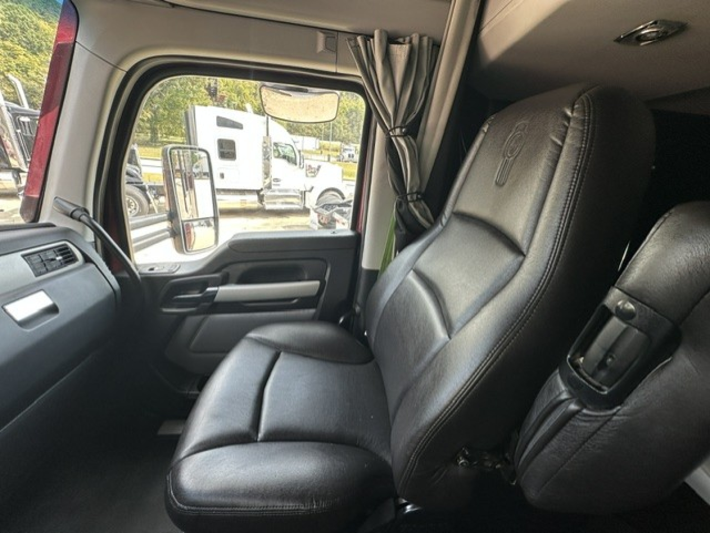 Kenworth T680 cab interior showing driver seat and passenger seat, black leather upholstery, door panel, side mirror visible through window.