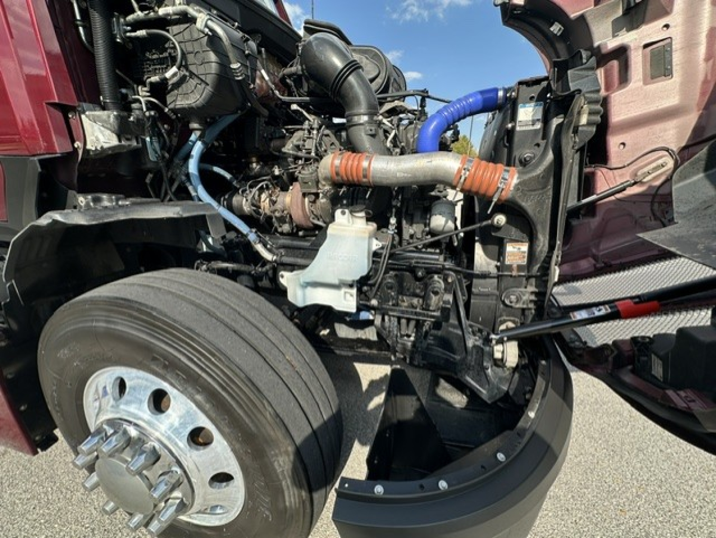Kenworth T680 engine bay showing front axle and intake hoses with orange and blue clamps.