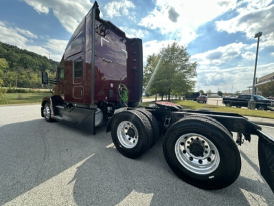 Kenworth T680 cab and dual rear axles of truck chassis showing polished wheels and brown maroon sleeper cab with side mirror, clear sky.