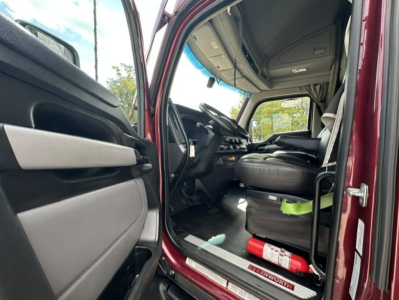 Kenworth T680 truck interior with open driver door showing steering wheel, dashboard, and seat; fire extinguisher visible on floor, door sill plate, and window view.