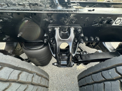 Kenworth T680 undercarriage view showing rear suspension hanger and dual rear wheels, underframe with brackets and bolts, engine bay area not visible.