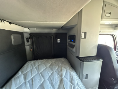 Interior sleeper area of a 2023 Kenworth T680 cab showing a raised bed with quilted mattress and surrounding storage compartments.