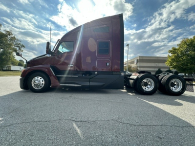 Kenworth T680 tractor cab side view showing maroon exterior and sleeper cab, 6-wheel rear chassis, black frame, daytime with blue sky.